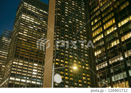 Multiple modern skyscrapers rise closely together in Midtown Manhattan, their windows glowing with artificial light. The night scene reflects the non-stop energy of New York City's business district. Multiple modern skyscrapers rise closely together in Midtown Manhattan, their windows glowing with artificial light. The night scene reflects the non-stop energy of New York City's business district. 126901712