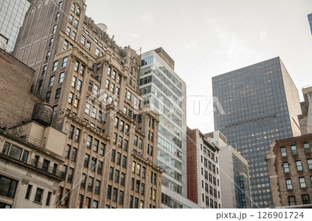 A row of historic brick buildings with detailed facades stands beside sleek modern glass towers in Midtown Manhattan. The late afternoon sun adds warmth to the architectural textures and contrasts. A row of historic brick buildings with detailed facades stands beside sleek modern glass towers in Midtown Manhattan. The late afternoon sun adds warmth to the architectural textures and contrasts. 126901724