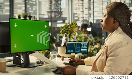 Employee at work using isolated screen PC display to finish project tasks. African american office clerk in workplace reading data statistics on mockup computer monitor, camera B Employee at work using isolated screen PC display to finish project tasks. African american office clerk in workplace reading data statistics on mockup computer monitor, camera B 126902751