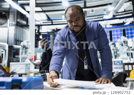 Black male sustainability consultant in suit evaluates solar panel systems and the production line in a modern factory, guiding operations toward clean energy and industrial efficiency. Black male sustainability consultant in suit evaluates solar panel systems and the production line in a modern factory, guiding operations toward clean energy and industrial efficiency. 126902752