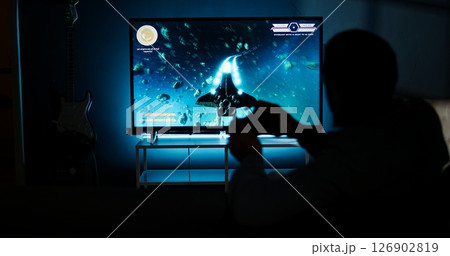 Young adult having fun with video games on his smart tv setup, connecting his console on lcd monitor television in living room and enjoying chill game night at home. African american gamer. Camera A. Young adult having fun with video games on his smart tv setup, connecting his console on lcd monitor television in living room and enjoying chill game night at home. African american gamer. Camera A. 126902819