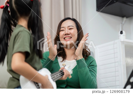 Music Education and Joyful Learning. A mother clapping and smiling while her daughter plays the ukulele. Music Education and Joyful Learning. A mother clapping and smiling while her daughter plays the ukulele. 126908179