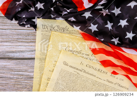Founding of Independence US documents are laid out on waving American flag, symbolizing national pride. 126909234