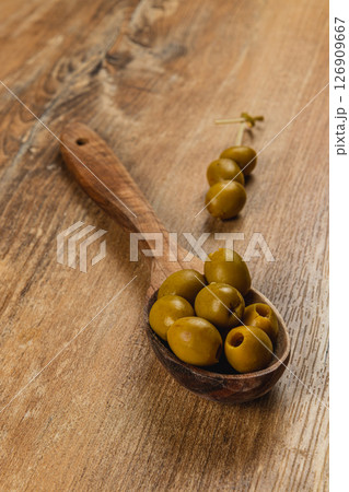 Wooden spoon filled with green olives on a rustic wooden table 126909667