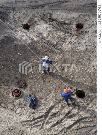 Top view of workers repairing underground heating mains through open hatches Top view of workers repairing underground heating mains through open hatches 126909743