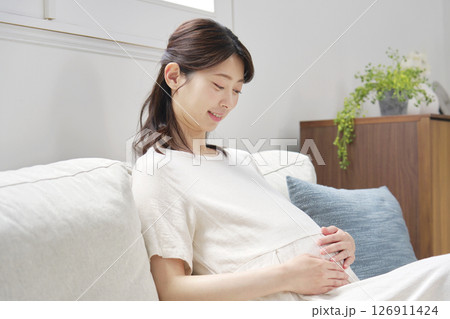 ソファーに座ってお腹を触る妊婦 126911424