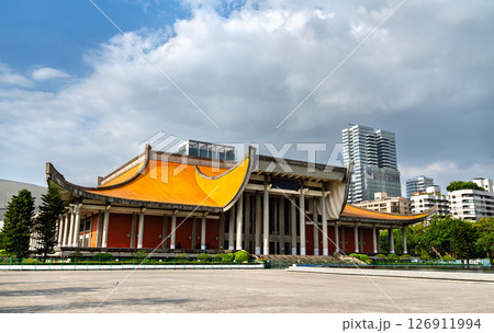 In Taipei, Taiwan, the Sun Yat-sen Memorial Hall shows its sweeping orange roof and concrete columns, contrasting with nearby high rises beneath dramatic gray clouds. 126911994