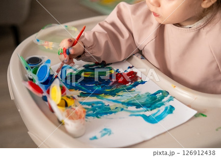 Little girl painting with gouache on a large sheet of paper. Joyful expression, creativity and early childhood development. Little girl painting with gouache on a large sheet of paper. Joyful expression, creativity and early childhood development. 126912438