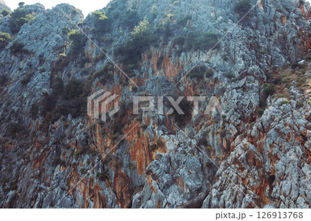 A relief coastal cliff with a distinctive texture and bright natural shades. The stone surface with erosion cracks and sparse vegetation is washed by clear sea water. Sea voyage. 126913768