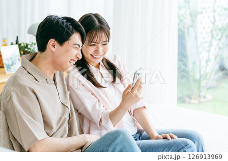 リビングでスマホを見るカップル リビングでスマホを見るカップル 126913969