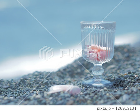 ピンク色の桜貝を入れたグラスを持つ手 126915131