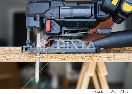 Close up of electrical handheld jigsaw cutting wooden board in workshop. Work tools for manual labor. Carpentry and woodworking concept 126917357