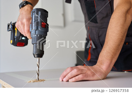 Male hands drilling wooden board with power drill. Process of carpentry working in home workshop, drills hole in chipboard 126917358