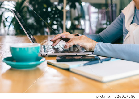 Hands of senior woman typing on laptop in cozy cafe with notebook and coffee 126917386