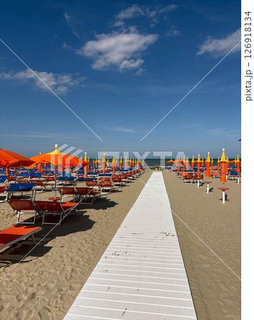 Sandy beach with empty sun loungers and orange umbrellas. Preparing for the beach season. 126918134