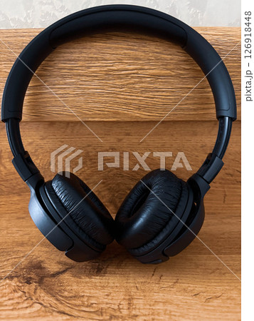 Black wireless headphones lie on a wooden shelf. 126918448