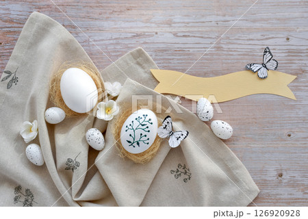 Stylish decorated easter eggs in nests on linen cloth on a light wooden background. Top view.  126920928
