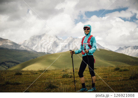 Tired woman trail runner running in grassland with snow capped mountains in the background 126921008