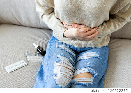 Caucasian female adult experiencing stomach pain on couch with medication nearby 126922275
