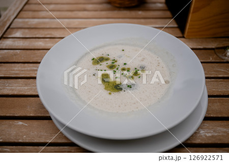 Creamy gourmet mushroom soup with herb oil on rustic wood table outdoors, concept of outdoor dining 126922571