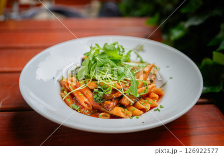 Penne pasta with tomato sauce and arugula served on white plate outdoors 126922577
