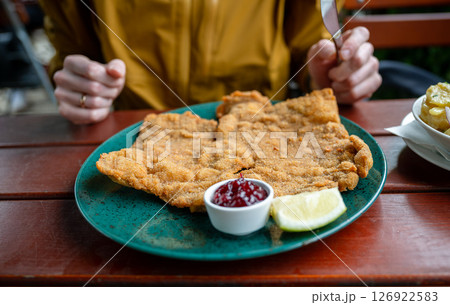 Breaded schnitzel with cranberry sauce and lemon slice on a green plate on a wooden outdoor table 126922583
