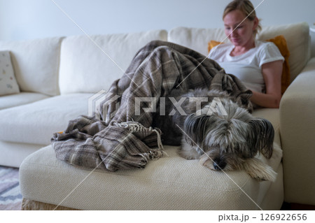 Woman relaxing with her dog on couch under blanket in cozy home interior 126922656