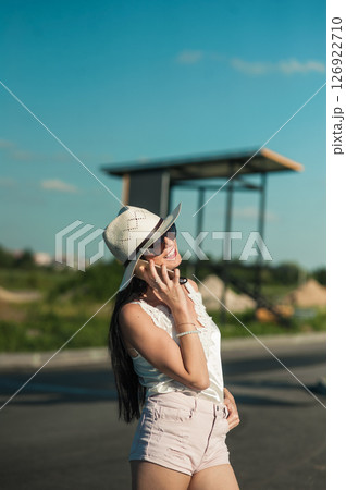 A young woman in a light white outfit is standing in the middle of nature and talking on the phone 126922710
