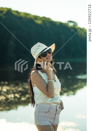 A young lady in a white outfit holding a phone to her ear is depicted near the water A young lady in a white outfit holding a phone to her ear is depicted near the water 126922718