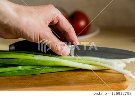 Men's hands hold a knife over green onions. 126922792