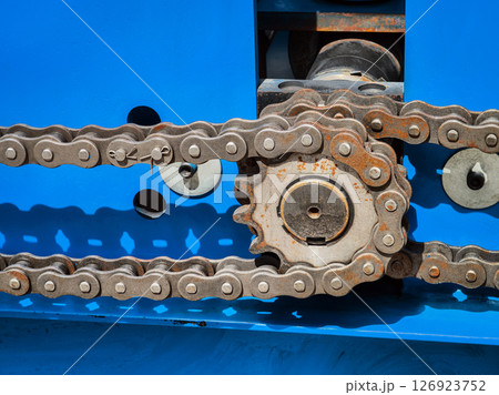 Close-up view of a rusted metal chain on machinery in an industrial setting during daylight hours 126923752