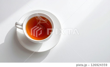 Steaming cup of black tea sits on white saucer, casting soft shadow on bright surface Steaming cup of black tea sits on white saucer, casting soft shadow on bright surface 126924359