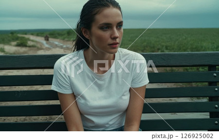 Young woman sitting on bench with her hair wet. She is wearing white T-shirt 126925002