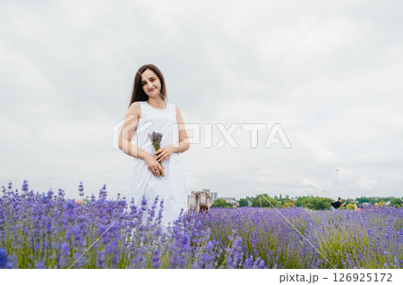 A young woman in a white dress stands in the middle of a lavender field 126925172