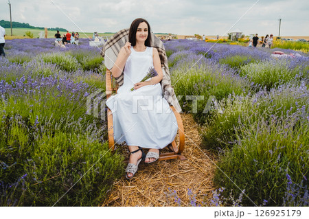 In the lavender field, there is a rocking chair where a charming woman sits 126925179