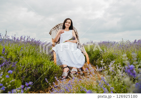 In the lavender field, a young woman in a white dress is sitting 126925180