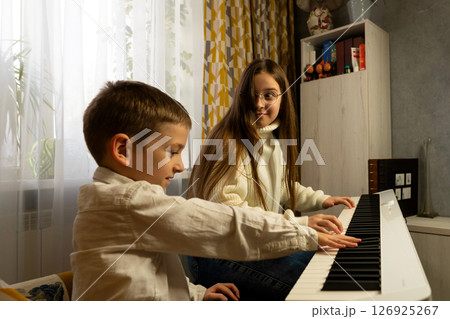 Boy presses piano keys while girl watches in surprise. 126925267