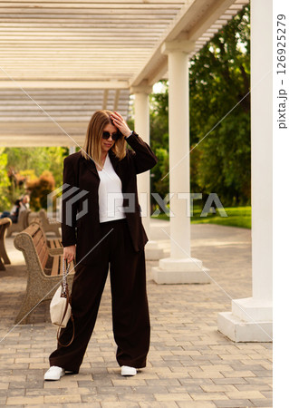 Young woman adjusts hair outdoors under white pergola structure. Young woman adjusts hair outdoors under white pergola structure. 126925279