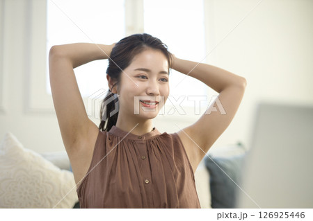 リビングでノートパソコンを見ながら伸びをする20代女性 126925446