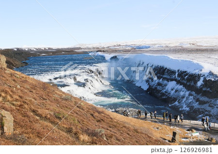horizontal photo took in Gullfoss Falls, Hvita river, Golden Circle, Reykjavik, Iceland. A waterfall cascading over rocky cliffs into a river below with snow covered areas and a clear blue sky horizontal photo took in Gullfoss Falls, Hvita river, Golden Circle, Reykjavik, Iceland. A waterfall cascading over rocky cliffs into a river below with snow covered areas and a clear blue sky 126926981