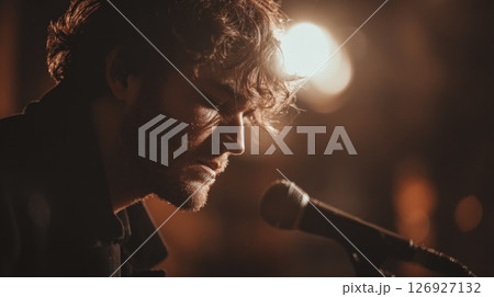 Young Musician Singing Into Microphone Under Warm Lighting At Concert Young Musician Singing Into Microphone Under Warm Lighting At Concert 126927132