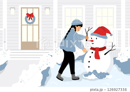 Girl building a snowman in front of a house in winter. Girl building a snowman in front of a house in winter. 126927338