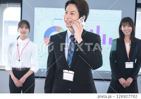会議室のスクリーンの前でスマホで話すスーツ姿の男性 126927782