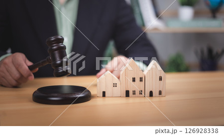 Hand with gavel near wooden houses. Symbolizes real estate law, property auctions, legal decisions, and housing market transactions. Ideal for mortgages, home ownership, investment, legal concepts now Hand with gavel near wooden houses. Symbolizes real estate law, property auctions, legal decisions, and housing market transactions. Ideal for mortgages, home ownership, investment, legal concepts now 126928338