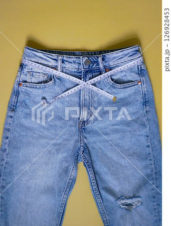 Female blue jeans with measuring tape flat lay on a yellow background. Losing weight, overweight and healthy lifestyle concept 126928453