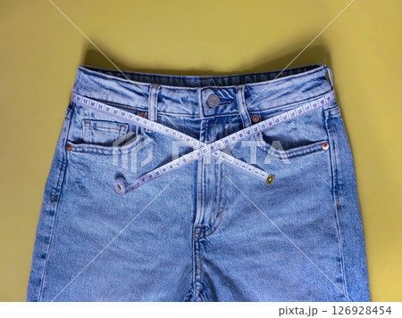 Female blue jeans with measuring tape flat lay on a yellow background. Losing weight, overweight and healthy lifestyle concept 126928454