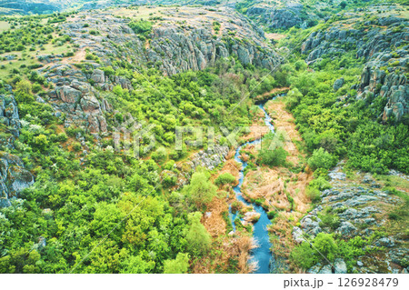 Aerial drone view of a stream running through a canyon in the mountains in the middle of a sunny summer day. 126928479