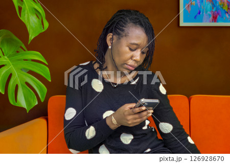 African Woman Texting on Smartphone While Sitting on Couch Indoors African Woman Texting on Smartphone While Sitting on Couch Indoors 126928670