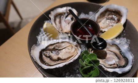 close up of four pieces of fresh raw oysters with vinegar and lemon slice on ice in a big plate with copy space 126928811