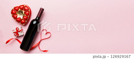 Bottle of red wine on colored background for Valentine Day with gift and chocolate. Heart shaped with gift box of chocolates top view with copy space 126929167